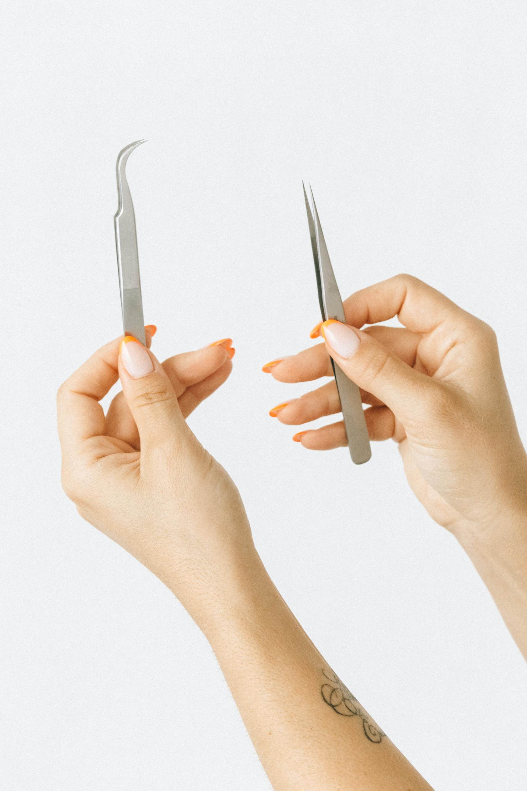 A pair of hands holding metal tweezers against a white background, showcasing manicure.