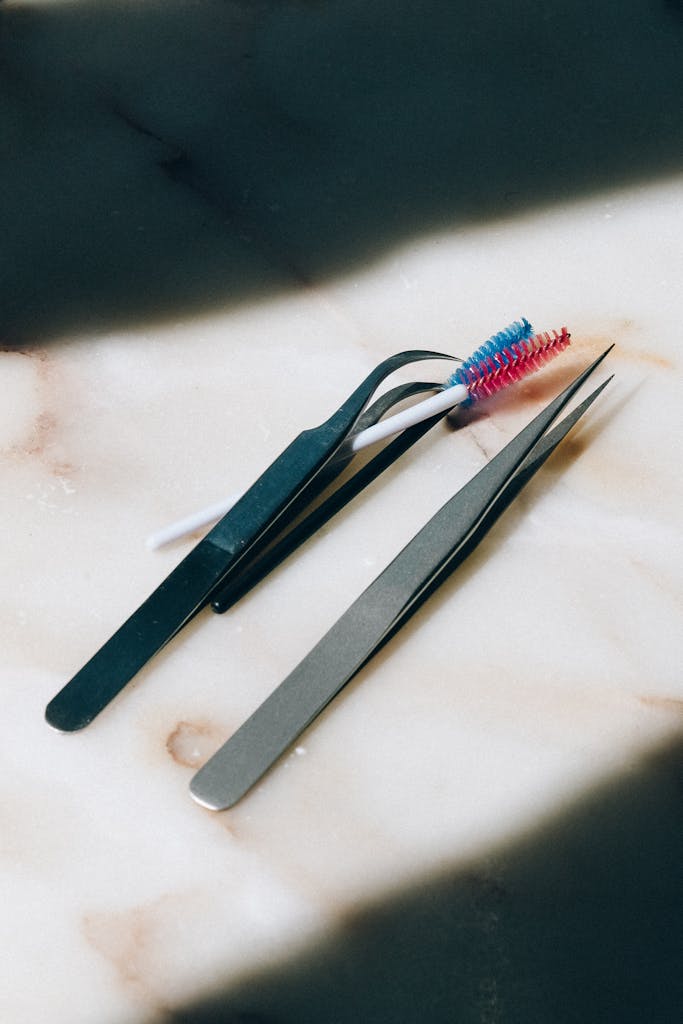 Close-up of tweezers and mascara brushes on a marble background.